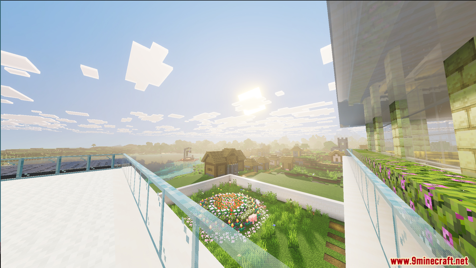 View from a glass balcony overlooking a flower garden and nearby village
